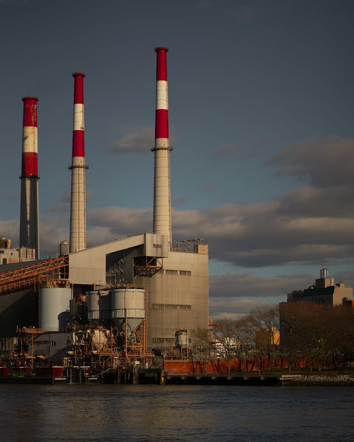 Crafting Captivating Headlines: Your awesome post title goes here Dramatic view of a power plant with red chimneys by a river, under a cloudy sky.