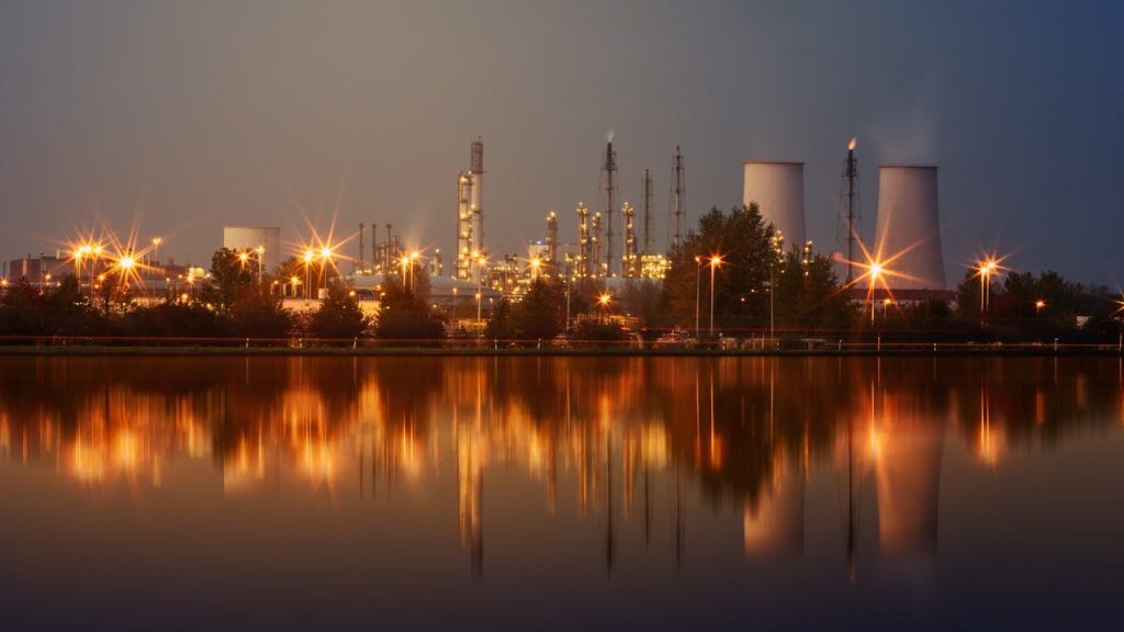Mastering the First Impression: Your intriguing post title goes here Industrial plant with reflection in water at twilight, showing smoke stacks and lights.